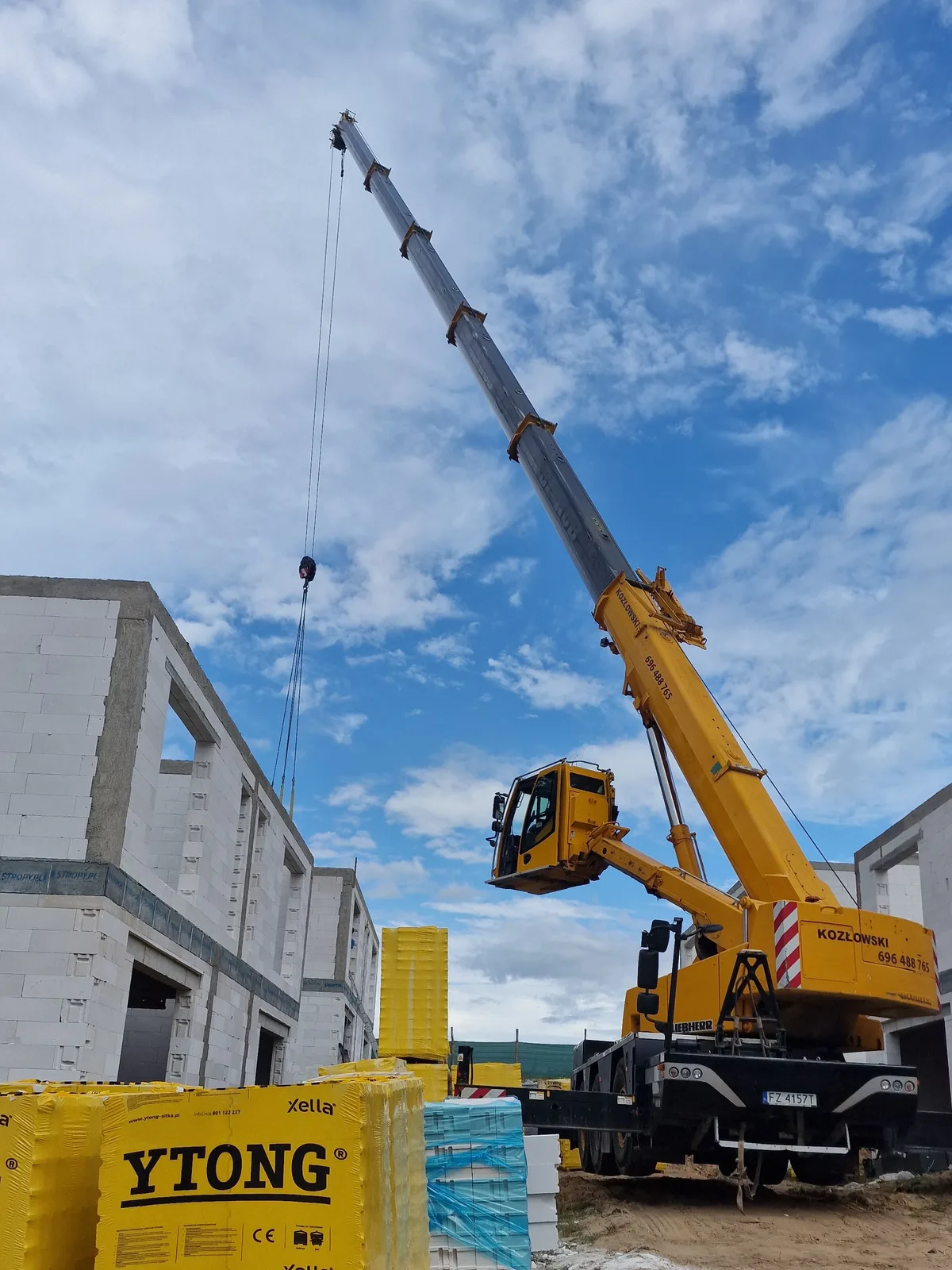 Żółty Liebherr LTC 1045-3.1 z pełnym wysięgiem podaje materiały na budowie osiedla, bloczki Ytong na pierwszym planie
